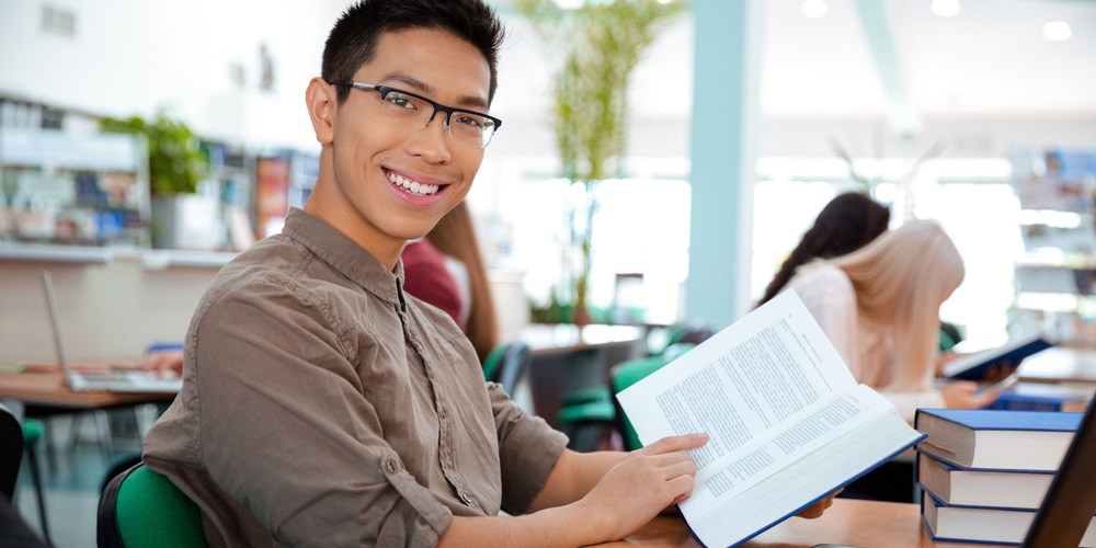 Portrait of a smiling asian man sitting at the table with book in university